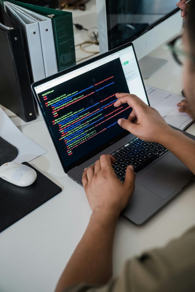 Close-up of a programmer pointing at a colorful code script on a laptop in an office setting.